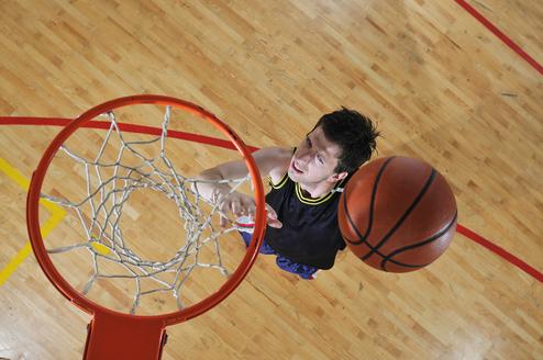 Junger Basketballspieler von oben, der einen Ball in den Korb wirft, vor einem Holzboden mit farbigen Linien.