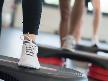 Nahaufnahme eines Fußs mit einem weißen Sport-Schuh auf einer Fitness-Stepp-Platte während eines Workout.