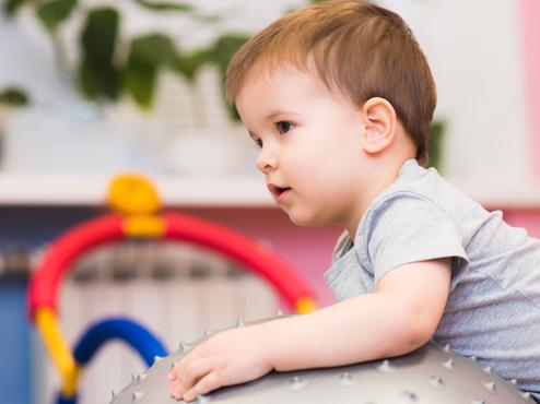 Kleines Kind sitzt auf einem großen, stacheligen Gymnastikball in einem bunten Spielzimmer.