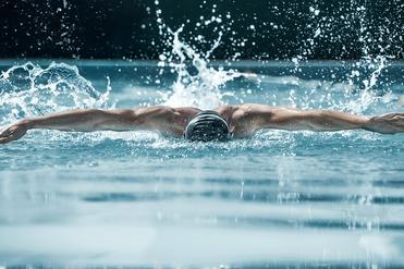 Schwimmer in einem blauen Pool macht einen Schmetterlingsschwimmzug, während Wasser spritzt und Bläschen aufsteigen.