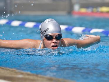 Junge Schwimmerin mit silberner Badekappe und Schwimmbrille in einem Wettkampfbecken, während sie einen Schlag ausführt.