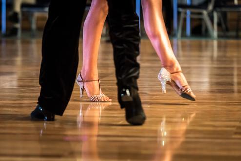 Nahaufnahme von tanzenden Füßen in eleganten Schuhen auf einem glänzenden Tanzboden.