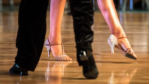 Nahaufnahme von tanzenden Füßen in eleganten Schuhen auf einem glänzenden Tanzboden.