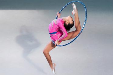 Mädchen in einem pinken Trikot springt mit einem Hula-Hoop-Reifen, während sie einen eleganten Tanzschritt ausführt.